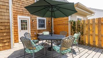 A wooden deck with a round table and four chairs, an umbrella, and a wooden fence.