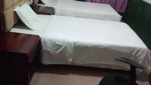 Een kamer met twee bedden, een houten nachtkastje en een zwarte bureaustoel.