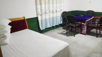 Una habitación con una cama, una mesa con sillas, un ventanal con cortinas y una pared verde.