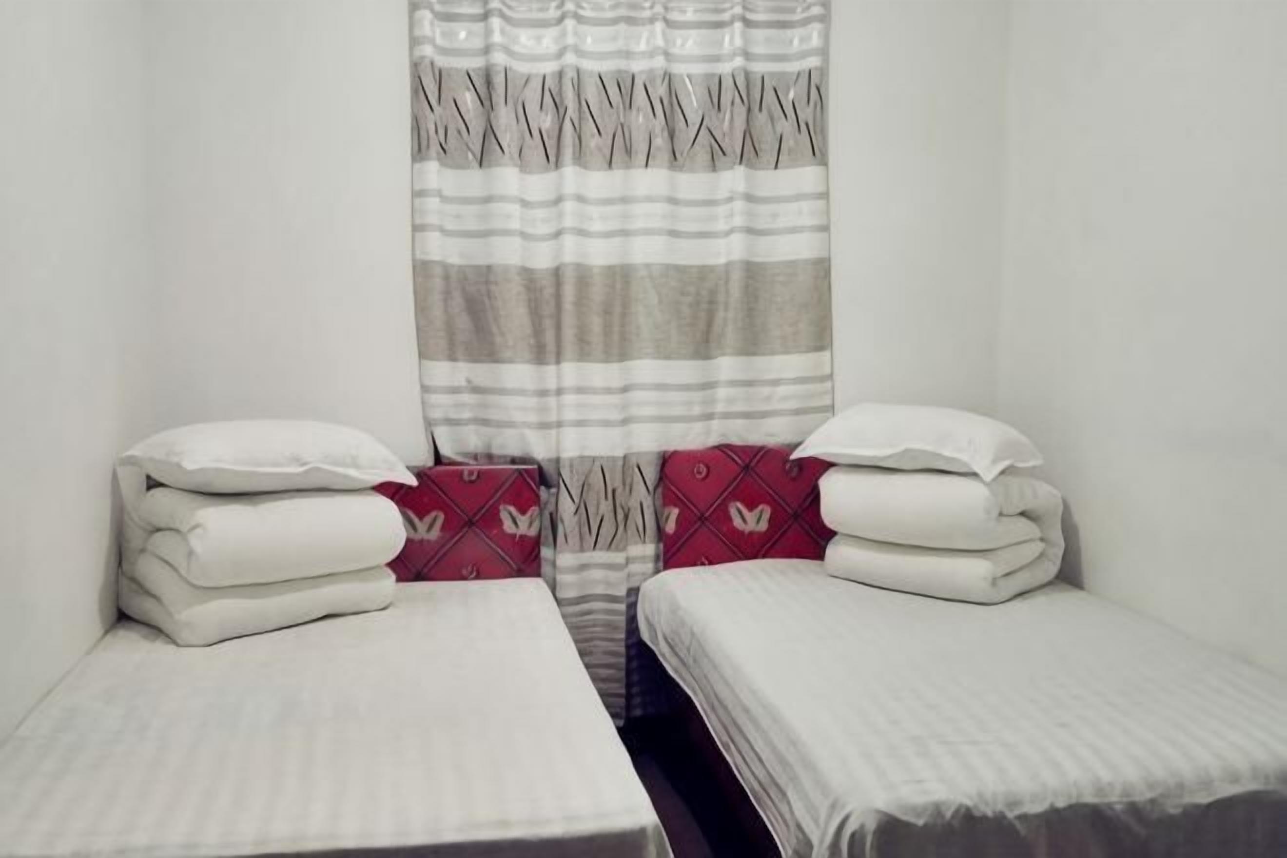 Een kleine, schone kamer met twee eenpersoonsbedden, een gestreept gordijn en een effen muur.