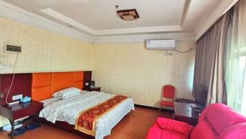 A hotel room with a bed, a desk, a chair, an air conditioning unit, and a window with curtains.