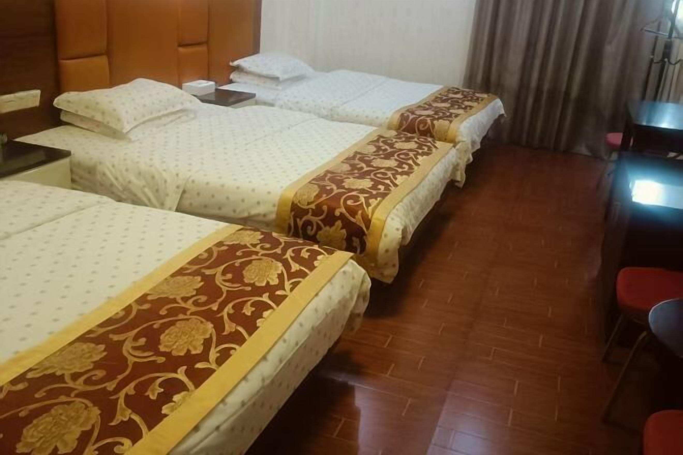 A hotel room with three beds, a wooden floor, a desk with a chair, and a window with curtains.