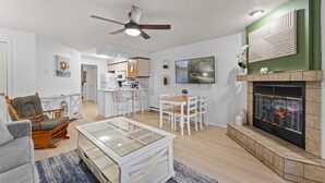 Een moderne woonkamer met een open haard, een eethoek en een keuken op de achtergrond.