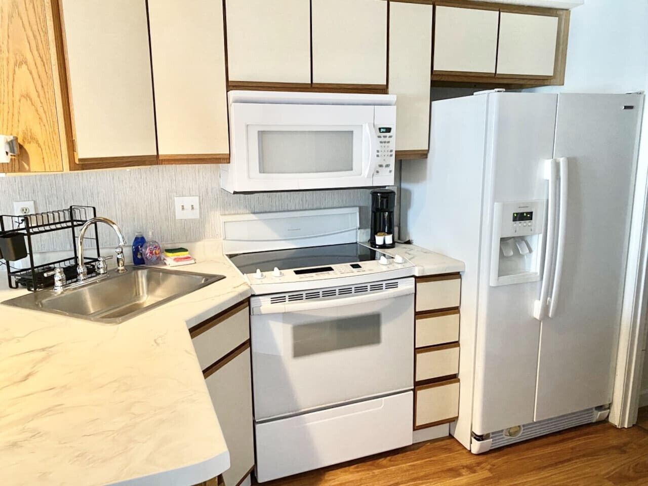 A compact kitchen with a stainless steel sink, a microwave, a built-in oven, and a white refrigerator.