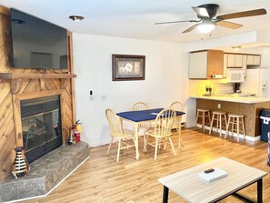 A living room with a fireplace, wooden dining table, and chairs. There is a kitchen area with a microwave and bar stools. - Dells Lake Lookout At Lighthouse Cove Condominiums (Wisconsin Dells)