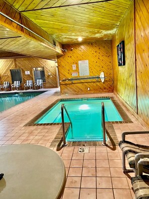 A pool area with tiled flooring, a pool with a blue water feature, and a wooden wall with a sign. - Dells Lake Lookout At Lighthouse Cove Condominiums (Wisconsin Dells)