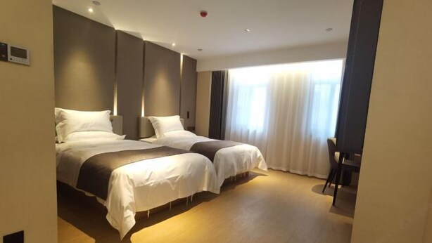 Une chambre d’hôtel moderne avec deux lits, une grande fenêtre avec des rideaux et une petite table.
