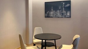 Une pièce moderne avec une table ronde et deux chaises, un tableau représentant un paysage urbain accroché au mur, et une palette de couleurs neutres.