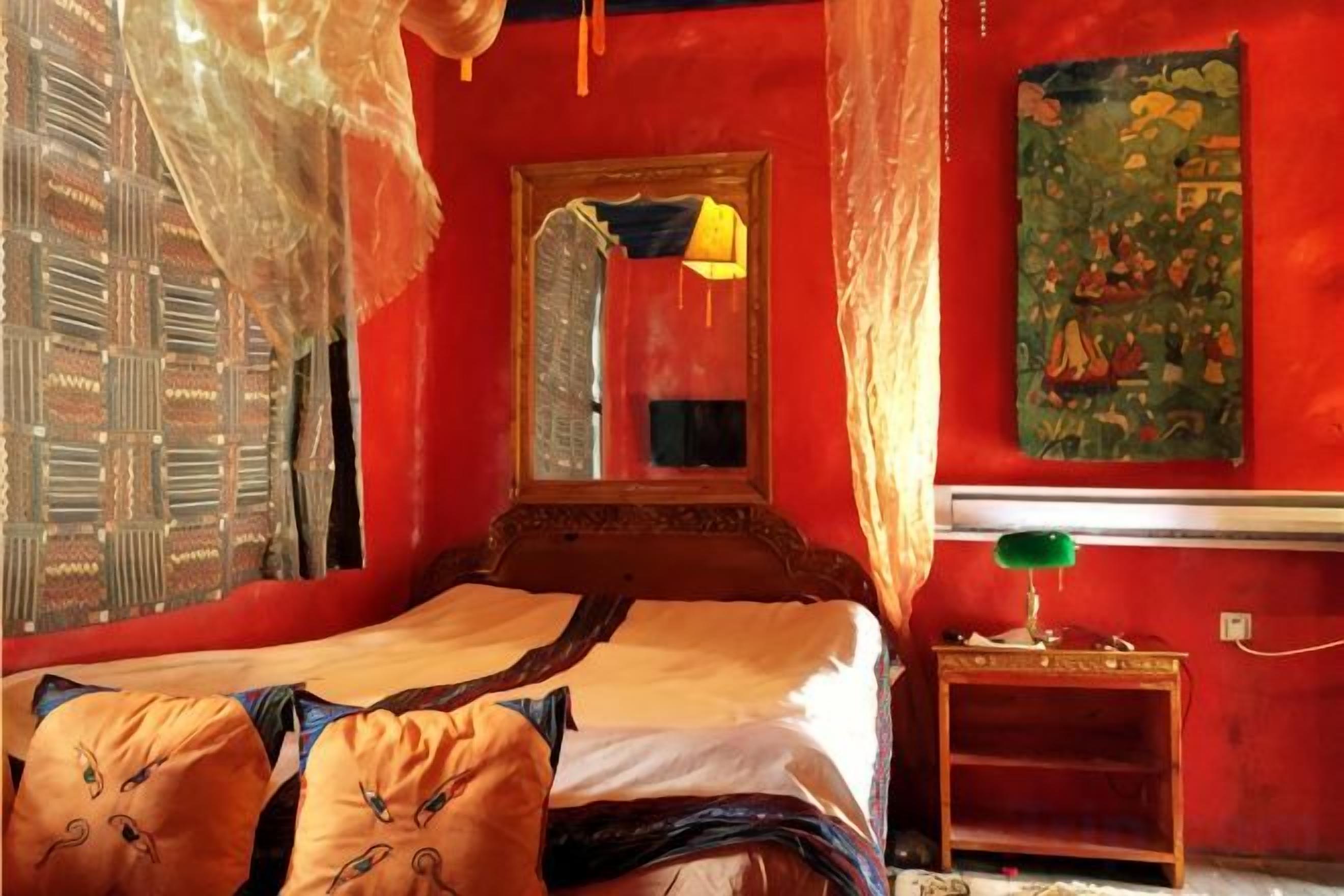 A room with a bed, a mirror, a green lamp, and a wall painting.