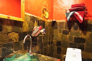 A bathroom with a stone wall, a green glass sink, a white sink, and a red towel rack.