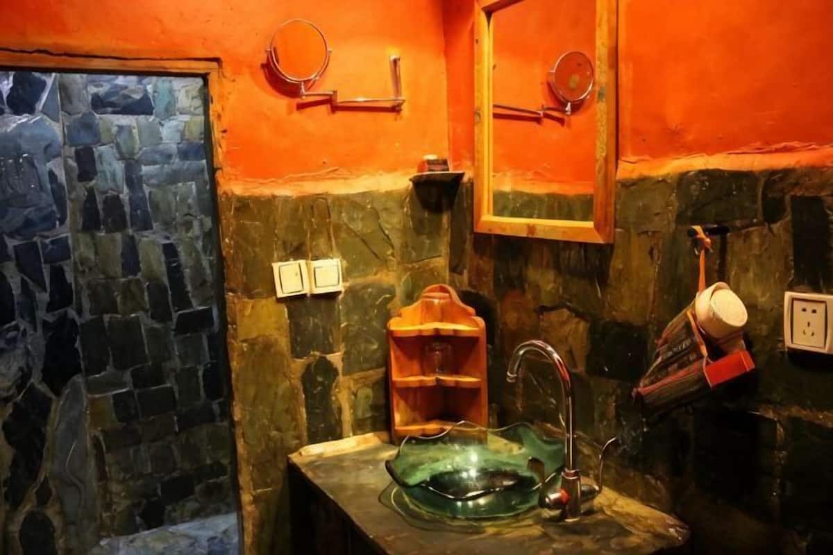 A bathroom with a stone wall, a glass sink, a mirror, and a red towel rack.