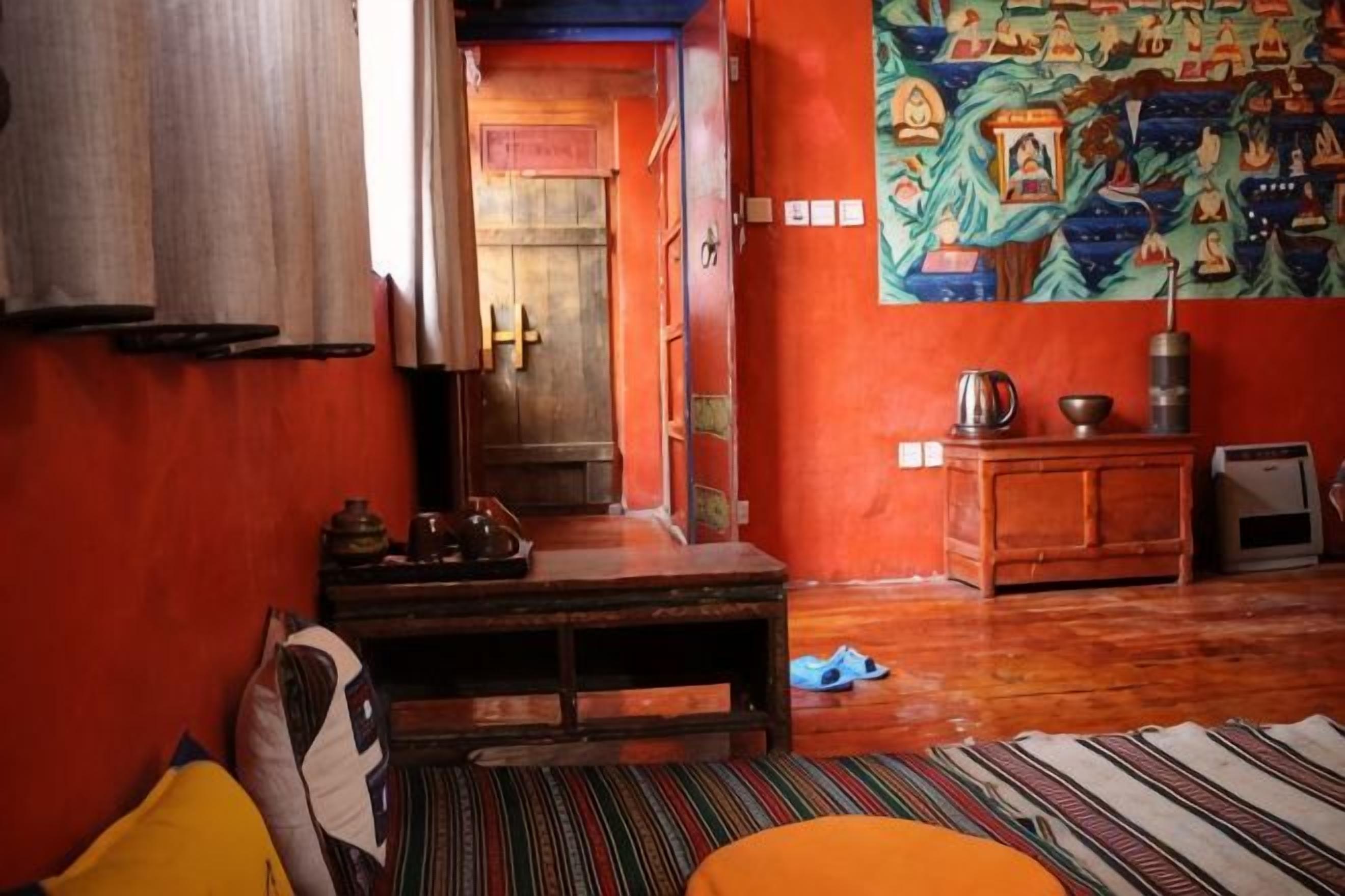 Une pièce comprenant un banc en bois, une petite table, une tapisserie colorée et une porte donnant sur une autre pièce.