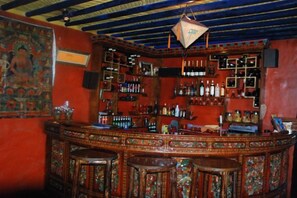 A bar with a wooden counter, multiple stools, and shelves stocked with bottles. - House of Shambhala Heritage Hotel (Lhasa)