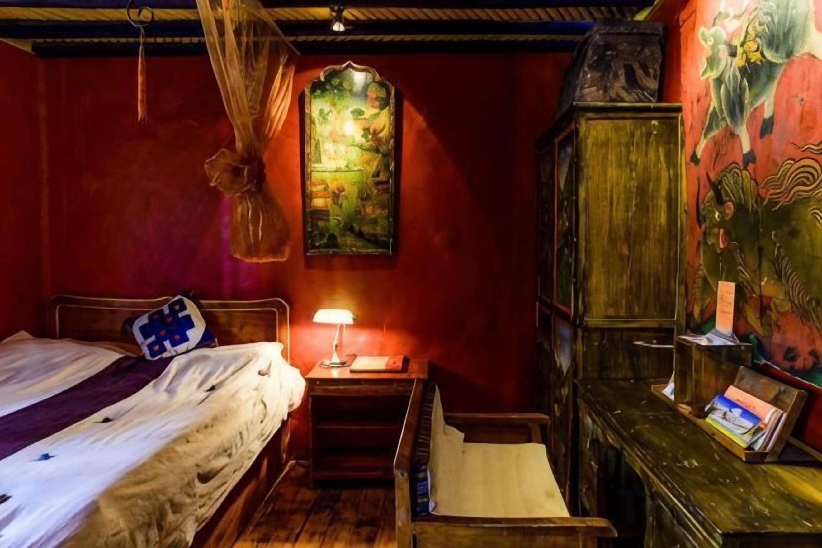 A room with a bed, a nightstand with a lamp, a wooden cabinet, and a wall with a painting.