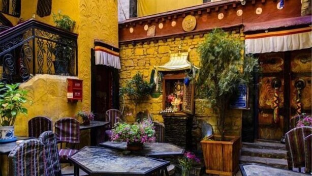 An outdoor café with stone walls, wooden furniture, and potted plants. - House of Shambhala Heritage Hotel (Lhasa)