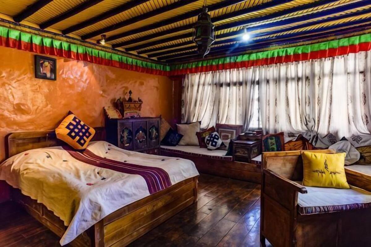A traditional room with a bed, a wooden chair, a small table, and a window with curtains.