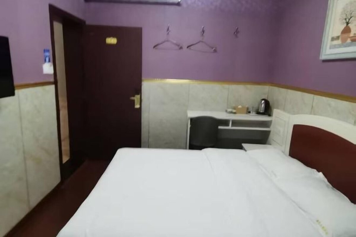 Une chambre d’hôtel équipée d’un lit, d’un bureau, d’une chaise et d’une petite table avec une bouilloire.