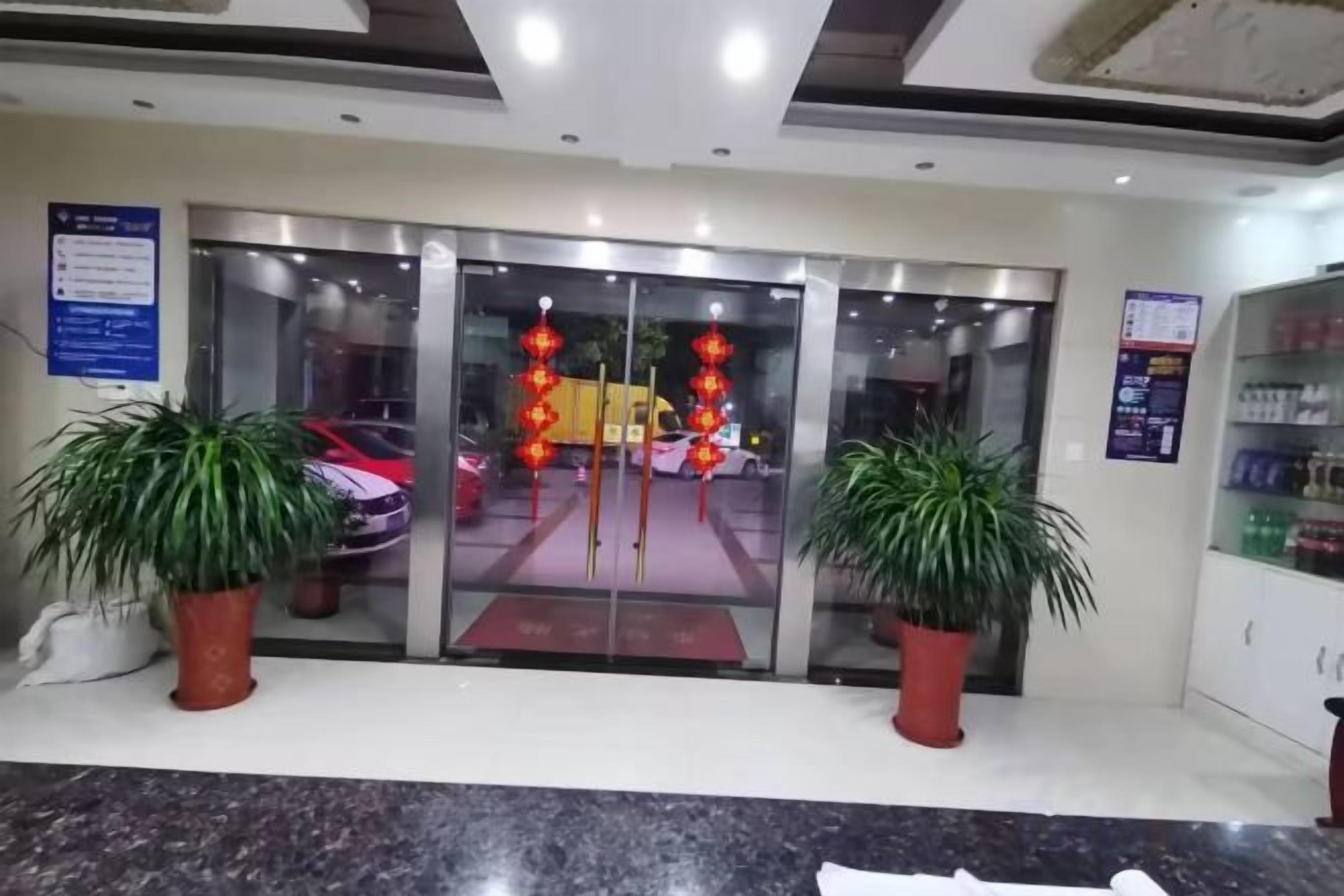 A hotel entrance with a glass door, potted plants, and a vending machine.