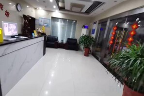 Een hotel receptie met een marmeren balie, zitplaatsen, een klok en potplanten.