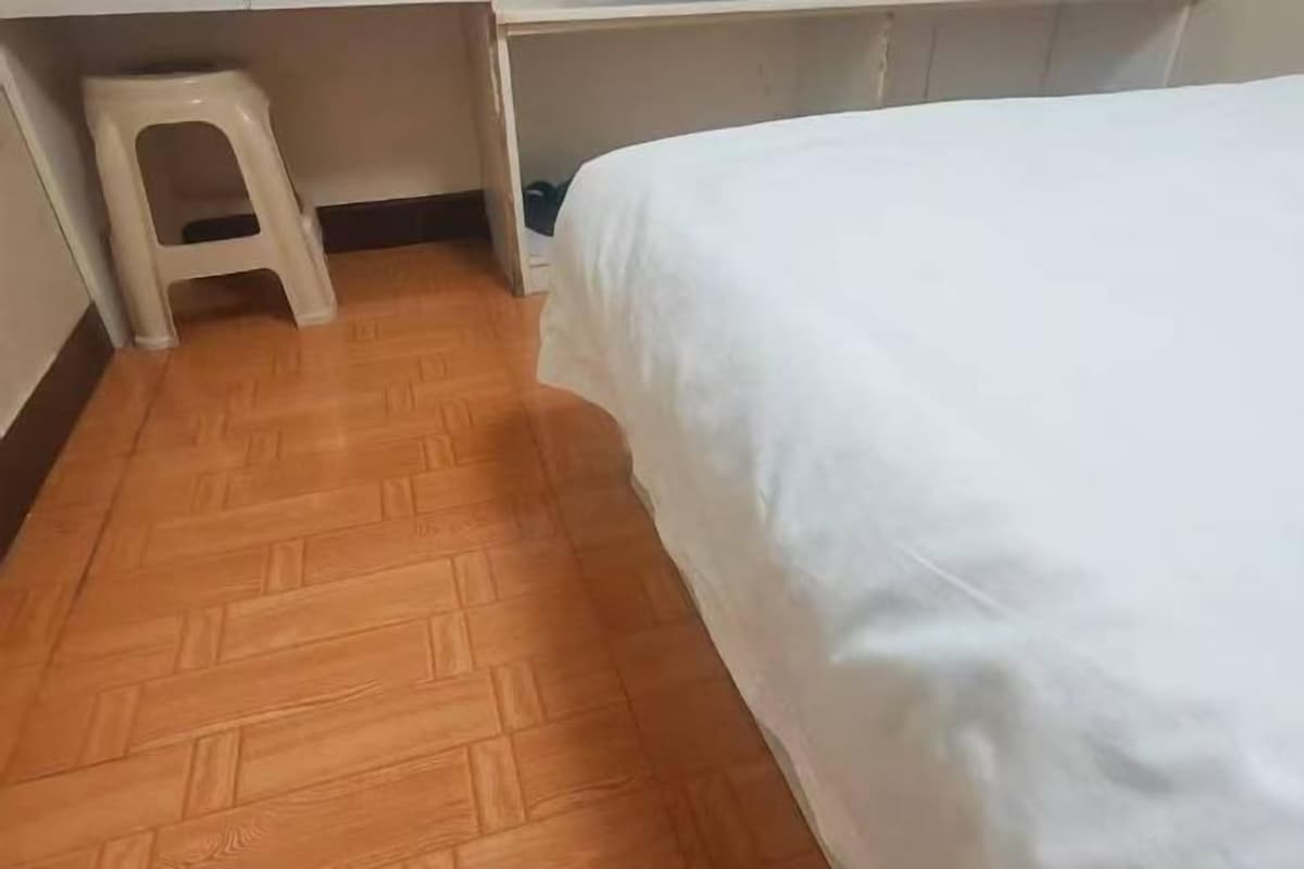 Una habitación con cama, piso de madera y un taburete pequeño.