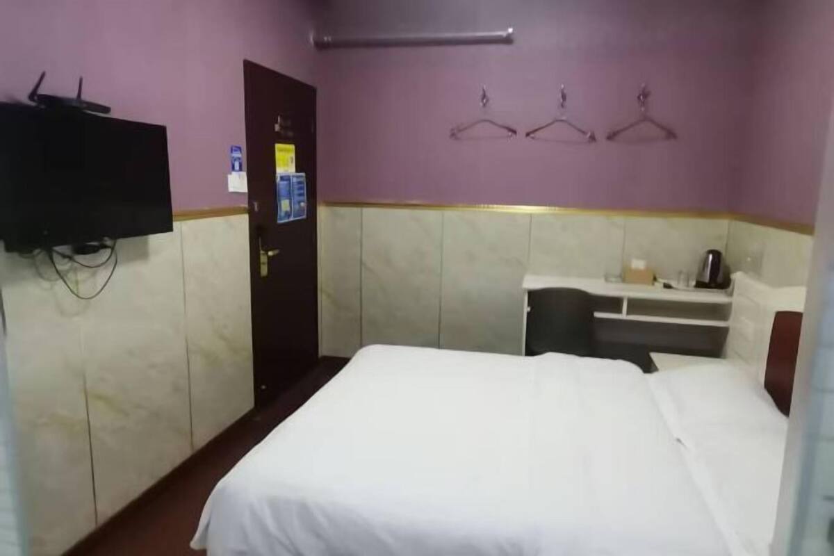 Een hotelkamer met een bed, een bureau met stoel, een aan de muur bevestigde televisie en een deur met een bordje.