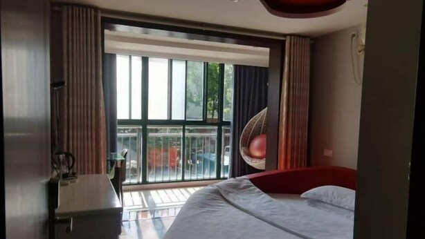 A modern hotel room with a large bed, a desk, and a balcony with a view of the outdoors. - Yancheng Xinyue Theme Hotel (Jiangsu Vocational College of Medicine Kangleyuan Branch) (Yancheng)