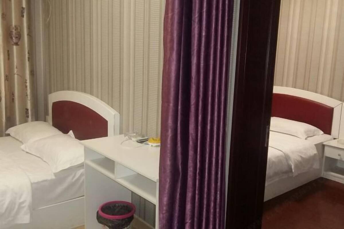 Een hotelkamer met twee bedden, een bureau en een prullenbak.