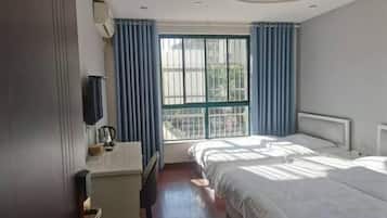 Una habitación de hotel con cama, escritorio, silla, televisor y ventana con cortinas.