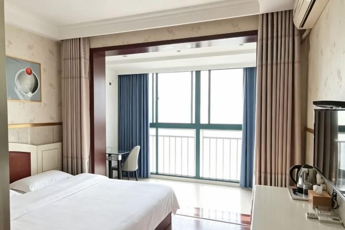 Une chambre d’hôtel avec un lit, un bureau, une chaise et un balcon avec des rideaux.