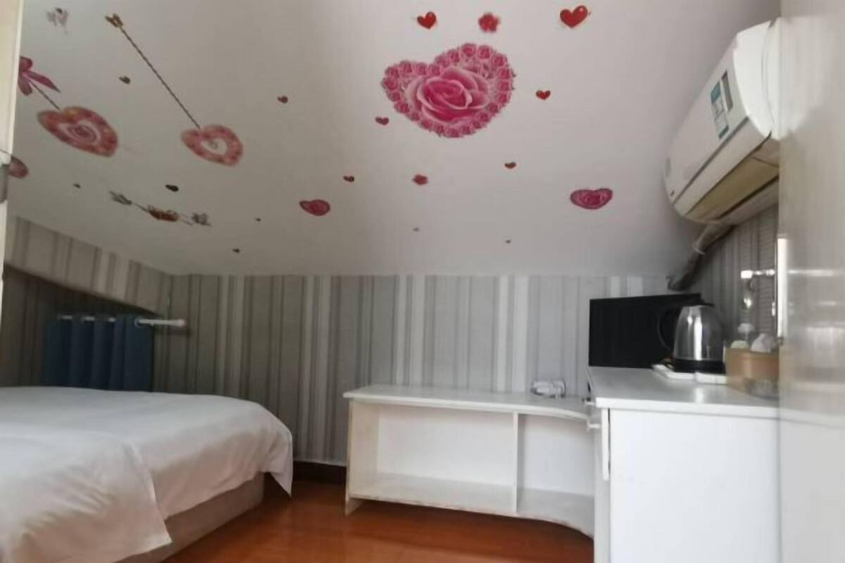 Een slaapkamer met een bed, een witte dressoir, een klein tafeltje en een plafond met bloem- en hartdecoraties.