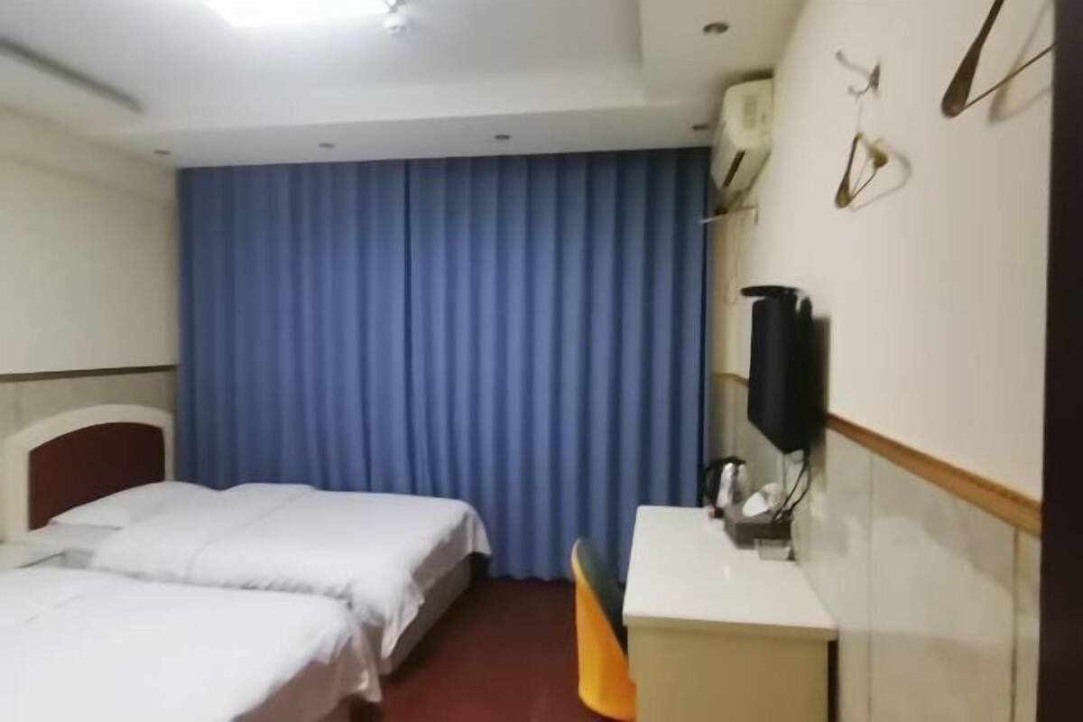 Een hotelkamer met twee bedden, een bureau, een stoel, een televisie en een gordijn.