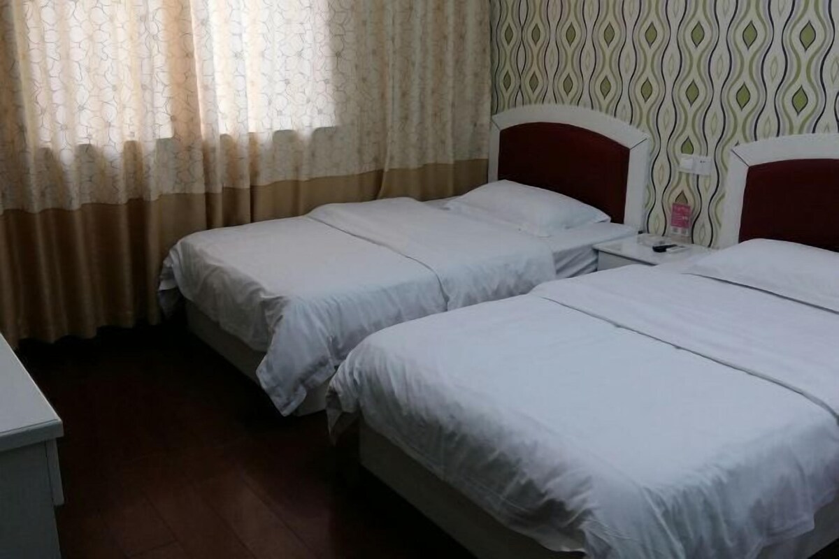 Habitación de hotel con dos camas individuales, suelo de madera, pared con diseño y ventana con cortinas translúcidas.