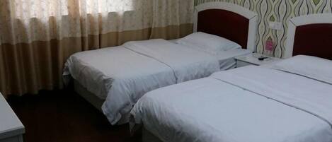 Habitación de hotel con dos camas individuales, suelo de madera, pared con diseño y ventana con cortinas translúcidas.