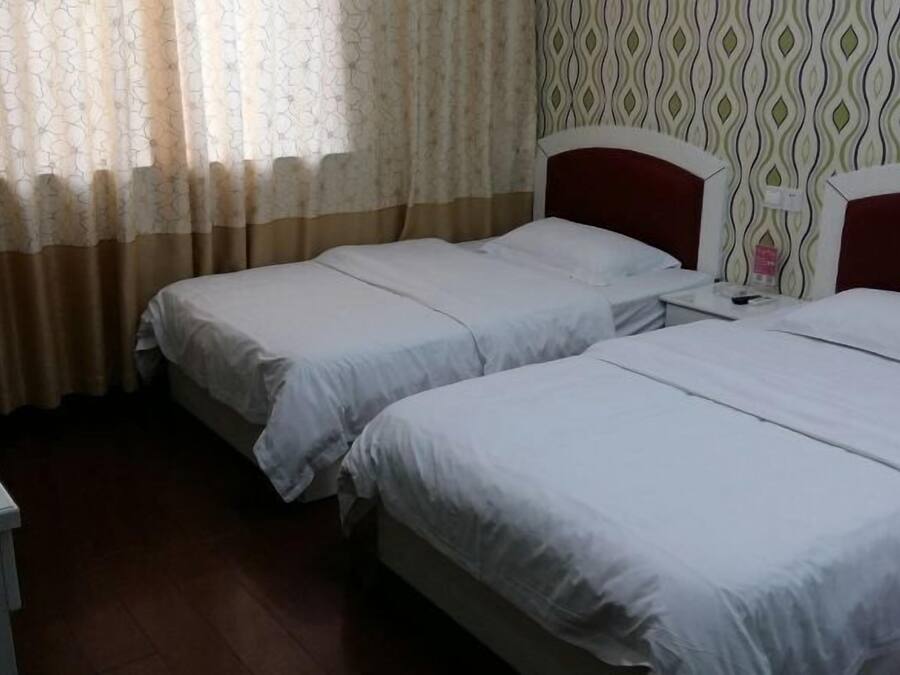 Habitación de hotel con dos camas individuales, suelo de madera, pared con diseño y ventana con cortinas translúcidas.