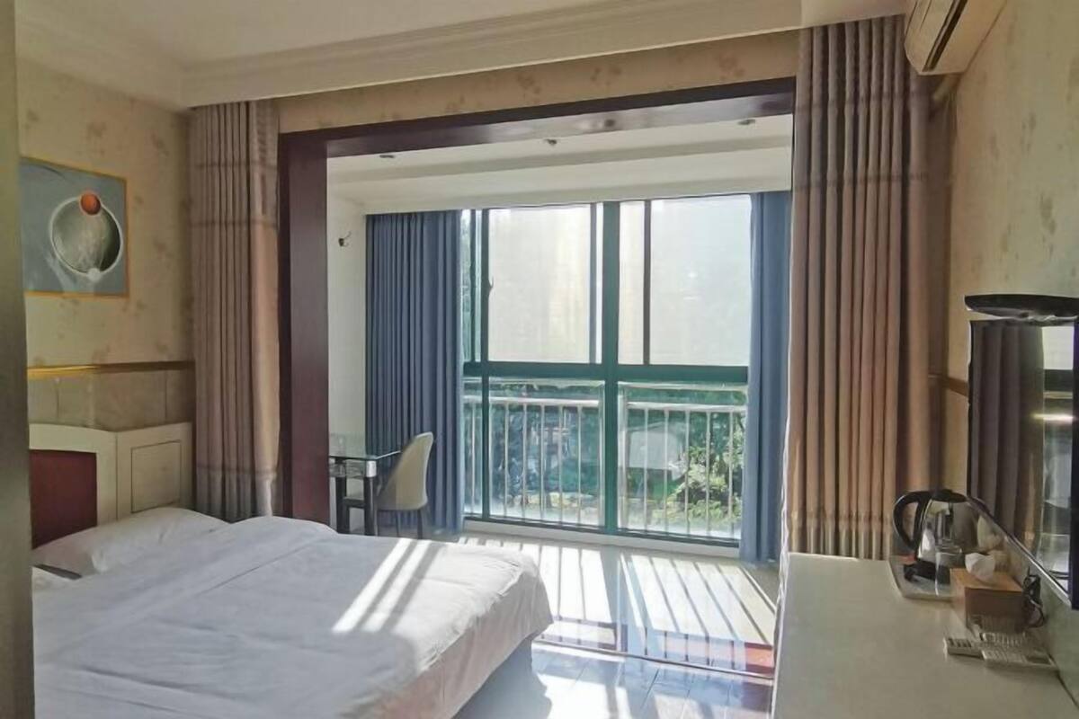 Een hotelkamer met een bed, een bureau, een stoel en een balkon met gordijnen.