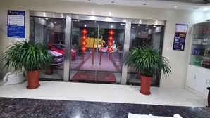 A hotel entrance with a glass door, potted plants, a reception desk, and a vending machine. - Yancheng Xinyue Theme Hotel (Jiangsu Vocational College of Medicine Kangleyuan Branch) (Yancheng)