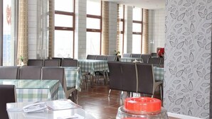 Um restaurante com várias mesas e cadeiras, janelas amplas e parede com padrão.