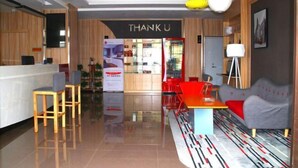 Uma área de recepção moderna com um balcão de madeira, um letreiro com a mensagem 'THANK U' e um espaço de espera com cadeiras vermelhas e um sofá cinzento.