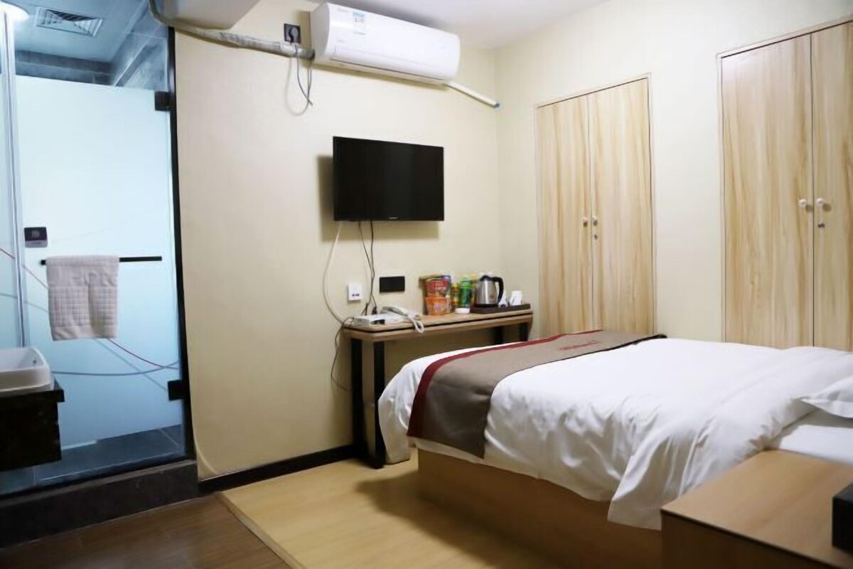 A hotel room with a bed, a TV mounted on the wall, a desk with a telephone and a coffee maker, and a wardrobe.