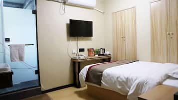 A hotel room with a bed, a TV mounted on the wall, a desk with a telephone and a coffee maker, and a wardrobe.