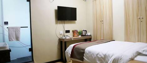 A hotel room with a bed, a TV mounted on the wall, a desk with a telephone and a coffee maker, and a wardrobe.