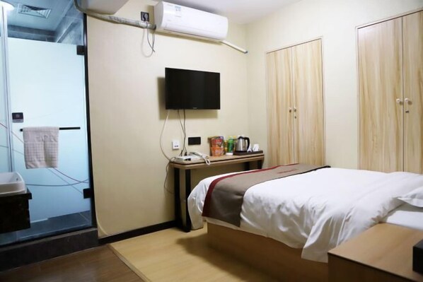 A hotel room with a bed, a TV mounted on the wall, a desk with a telephone and a coffee maker, and a wardrobe.