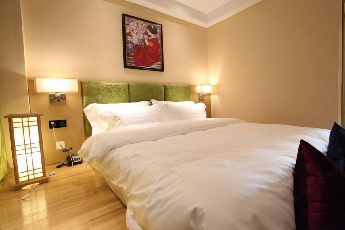 A hotel room with a large bed, two bedside lamps, a wall-mounted artwork, and a traditional Japanese-style floor lamp.