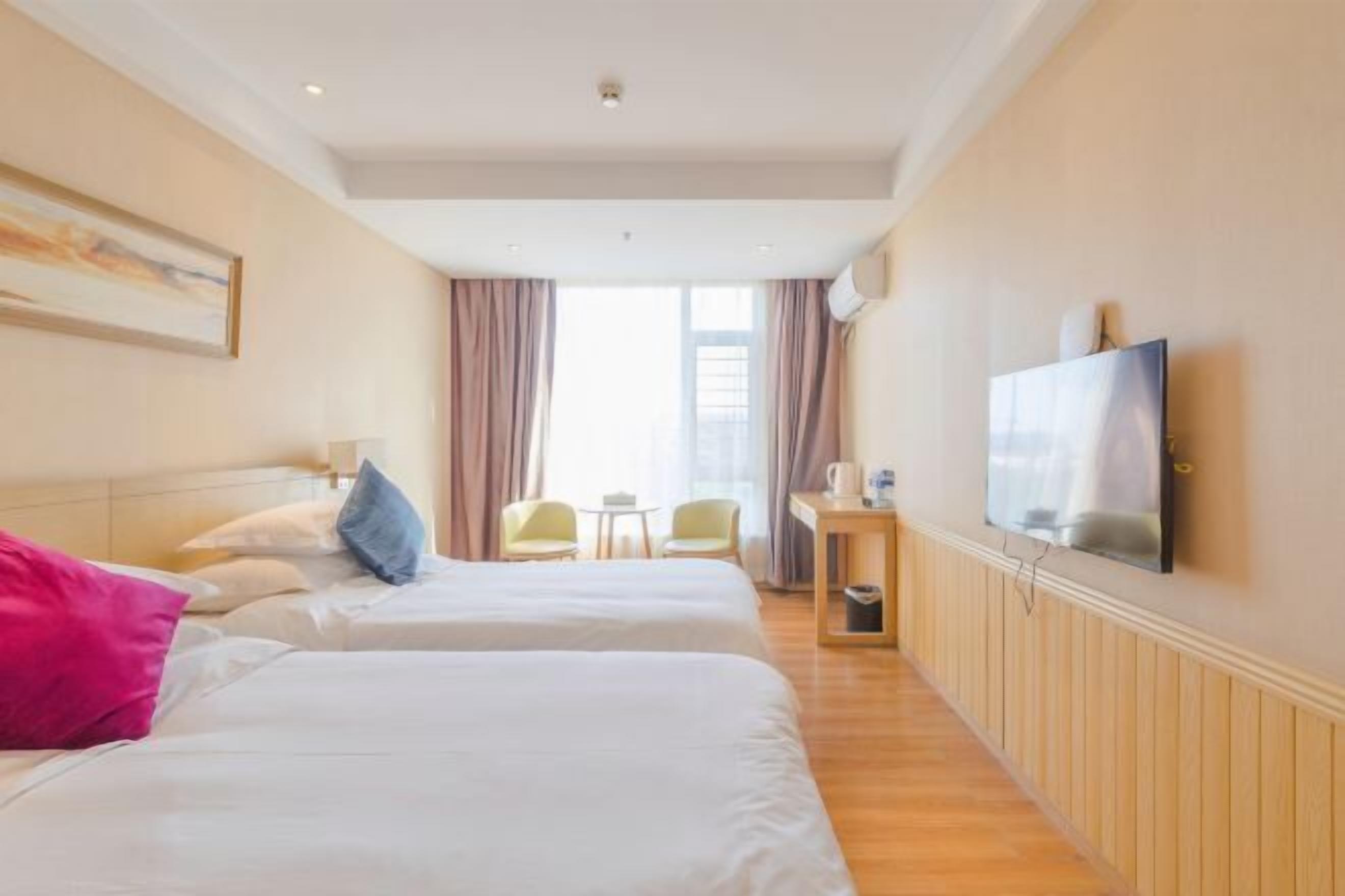 A hotel room with two beds, a television, a small table with a chair, and a window with curtains.