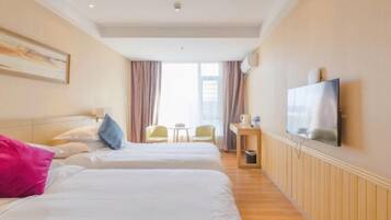 A hotel room with two beds, a television, a small table with a chair, and a window with curtains.