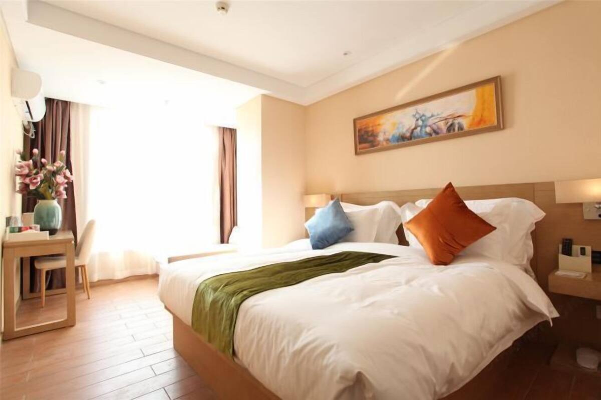 A hotel room with a bed, a desk, a chair, a painting on the wall, and a window with curtains.