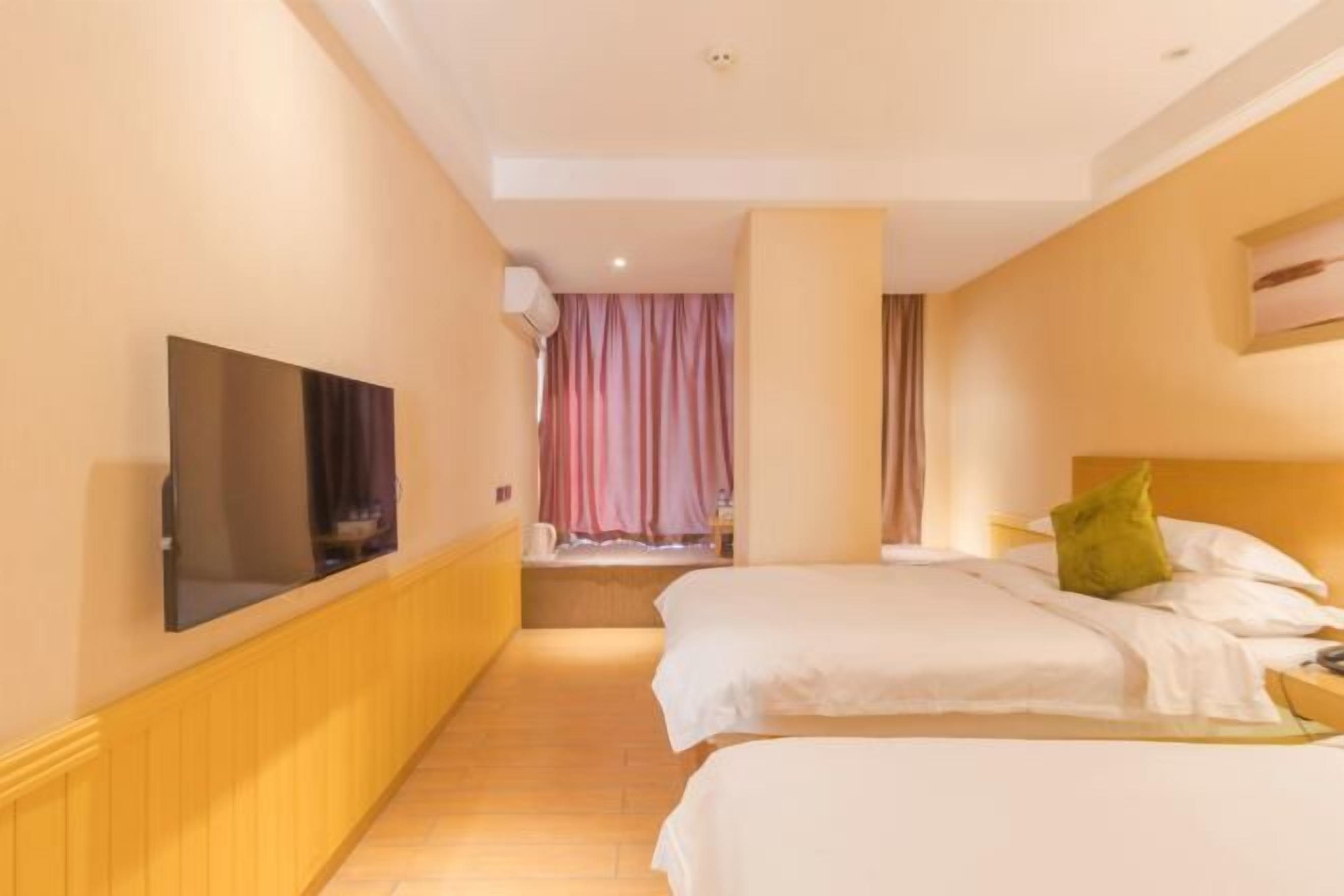 A hotel room with two beds, a television on the wall, and a window with curtains.