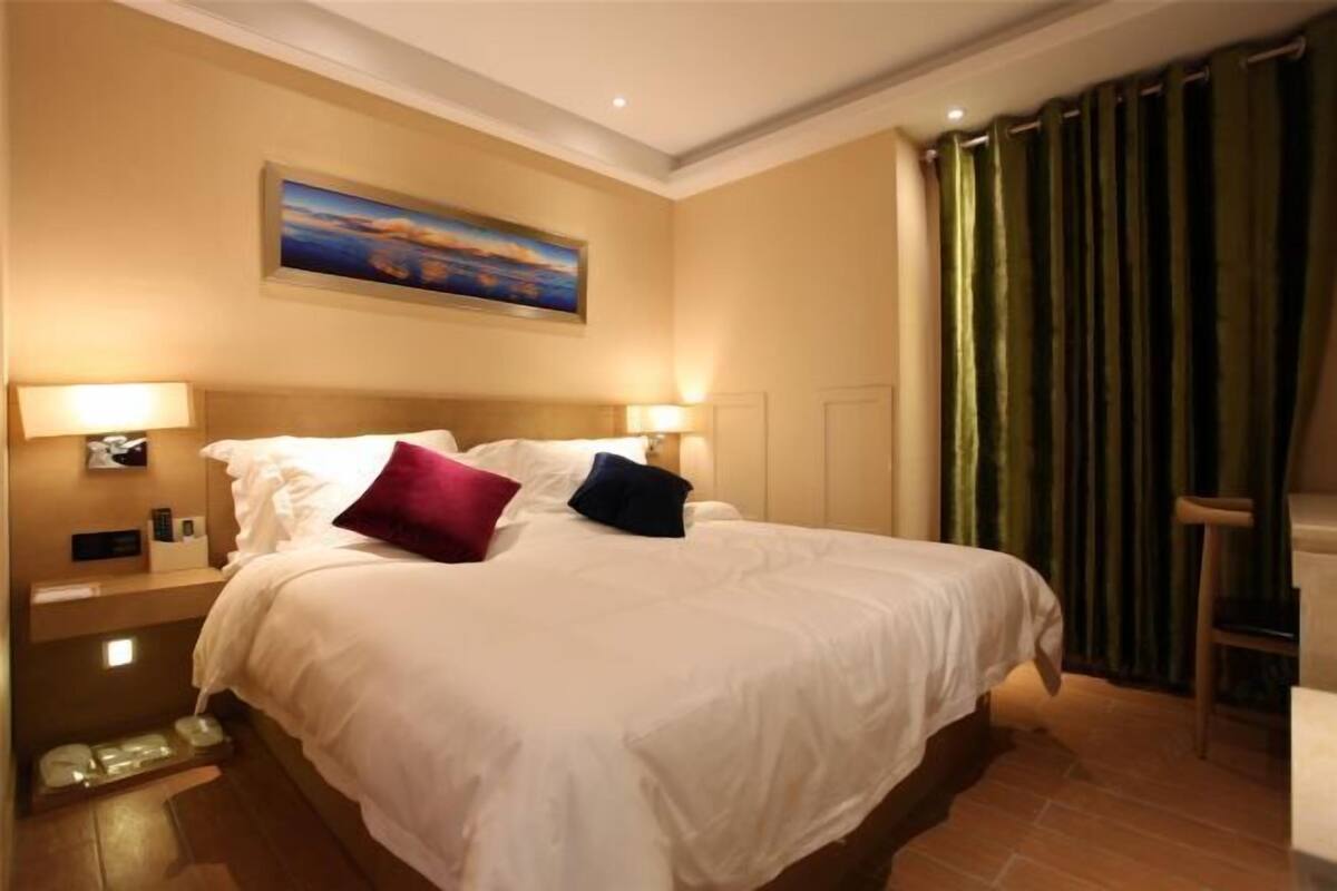 A hotel room with a large bed, two bedside lamps, a painting on the wall, and a green curtain.
