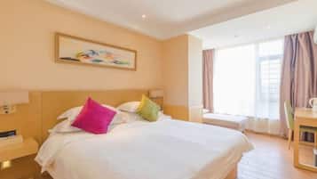 A hotel room with a large bed, a bedside table, a chair, a window with curtains, and a painting on the wall.