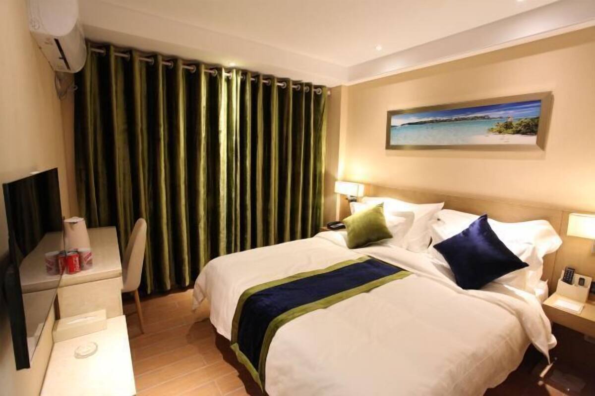 A hotel room with a bed, bedside tables, a desk, a chair, a painting on the wall, and curtains.